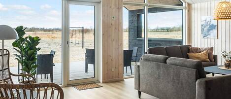 A modern interior with a grey sofa, wicker chairs, and a large window offering a view of the outdoors.