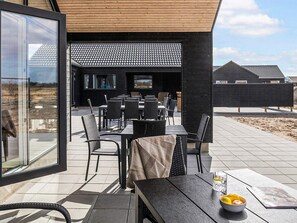 En udendørs patio med spisebord og stole, et fjernsyn og udsigt over det omkringliggende landskab.