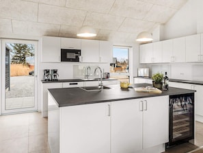 A modern kitchen with white cabinetry, a central island, a built-in oven, and a window overlooking a landscape. - 5 Star Holiday Home in Idestrup (Idestrup)