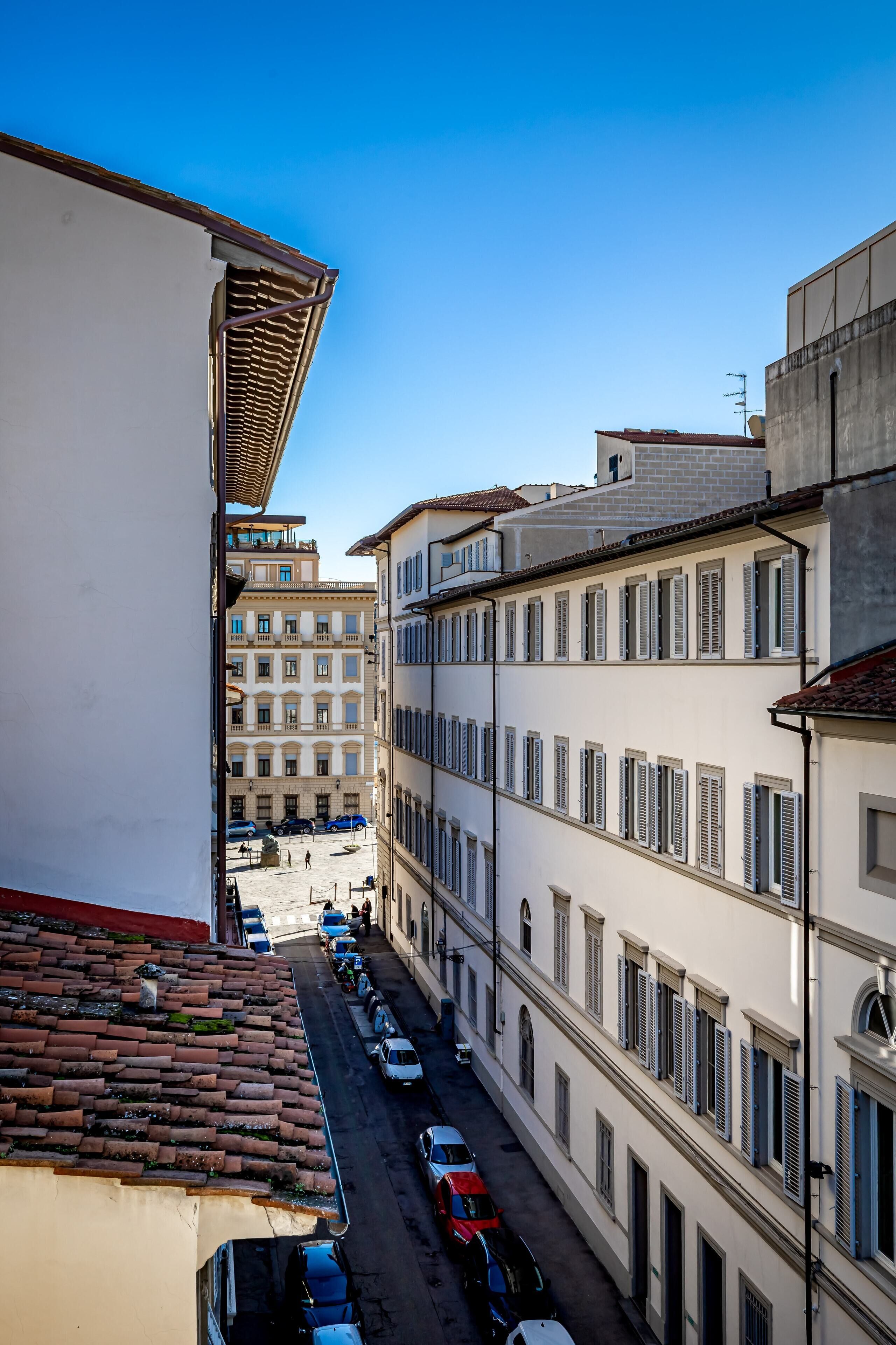 A narrow street with parked cars and buildings with uniform architecture.