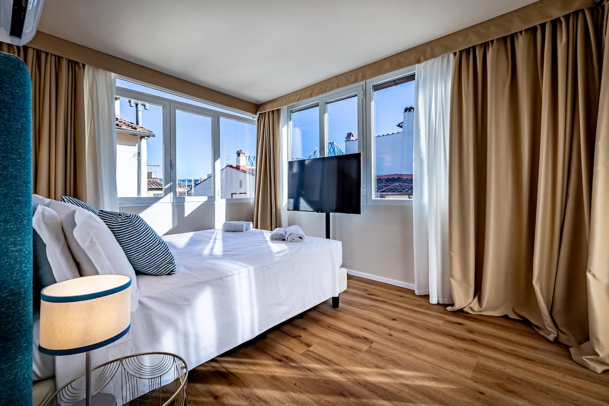 A hotel room with a bed, a TV, and large windows with curtains.