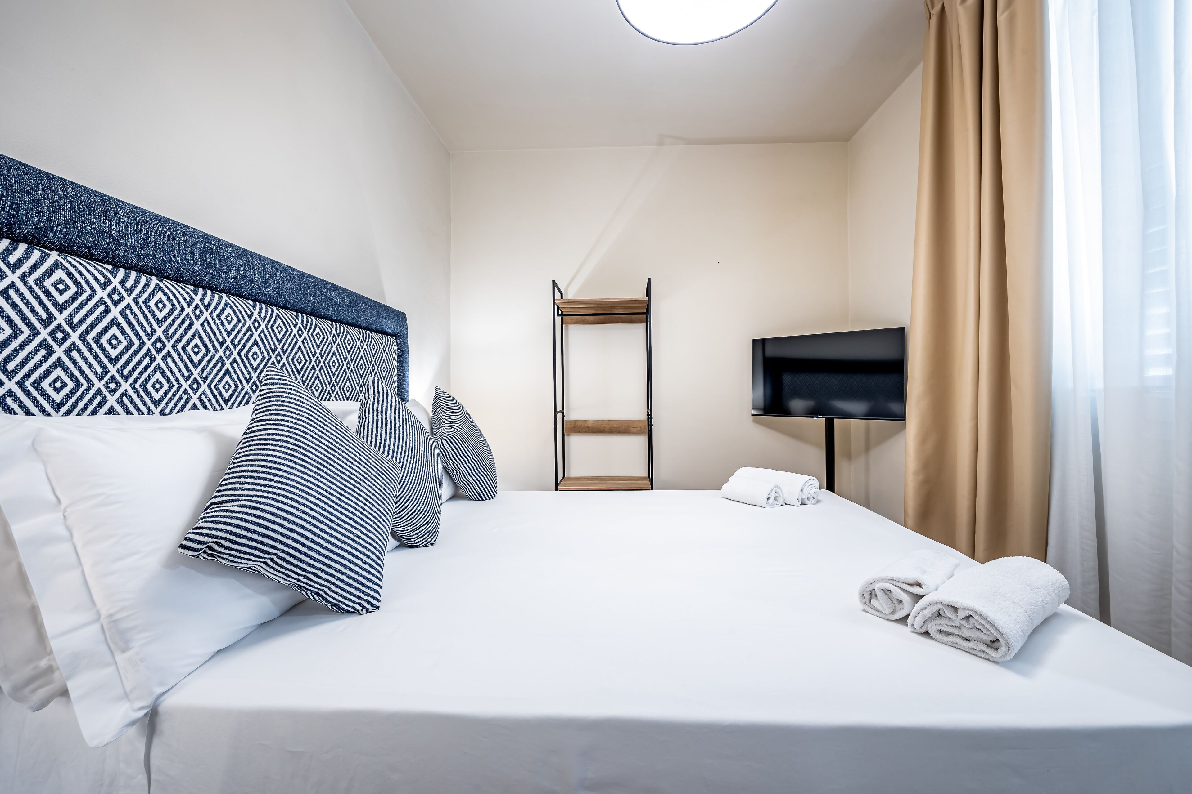 A hotel room with a neatly made bed, a television, and a wardrobe.