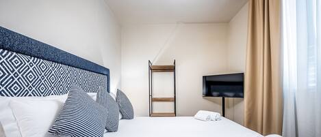 A hotel room with a neatly made bed, a television, and a wardrobe.