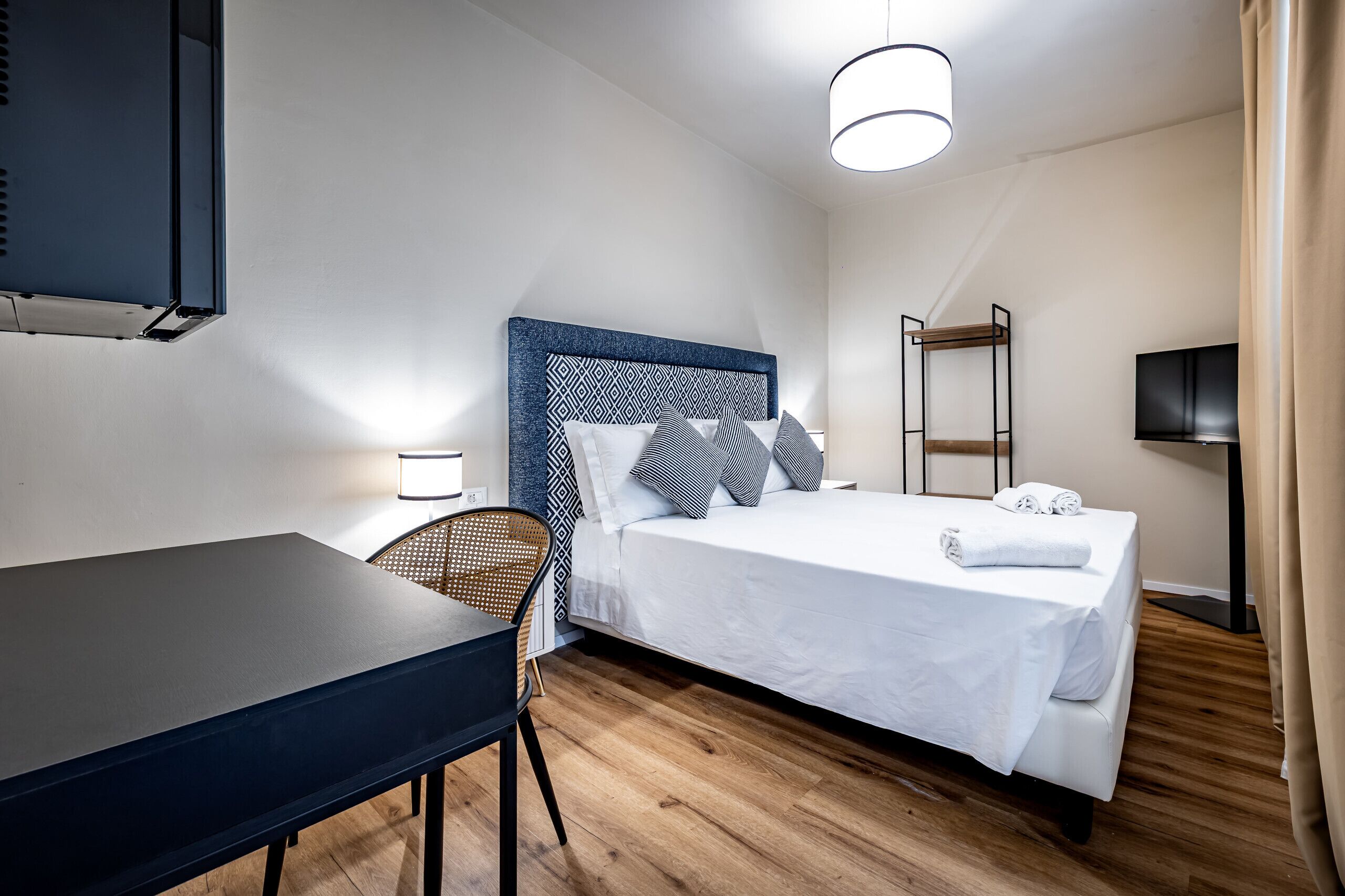 A hotel room with a bed, a desk, a chair, a TV, and a ladder.