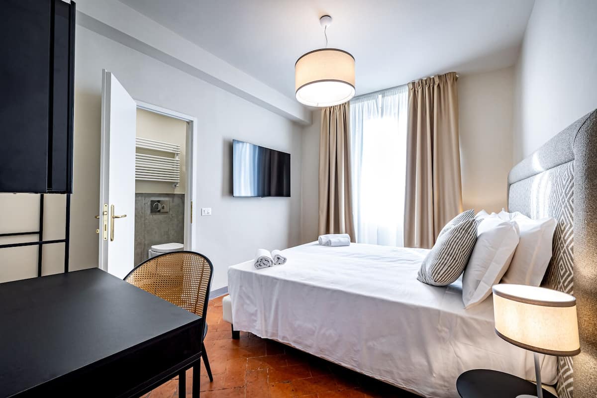 A hotel room with a bed, a TV, a desk, and a chair.