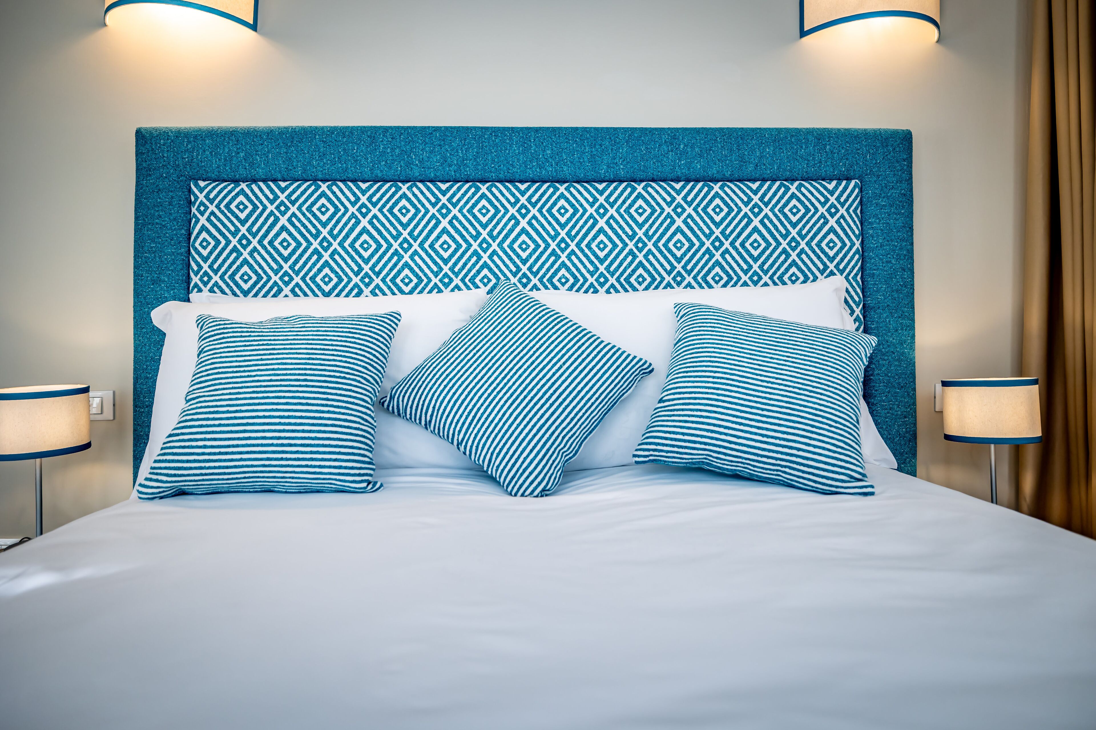 A neatly made bed with a blue and white patterned headboard, two bedside lamps, and a patterned pillow.