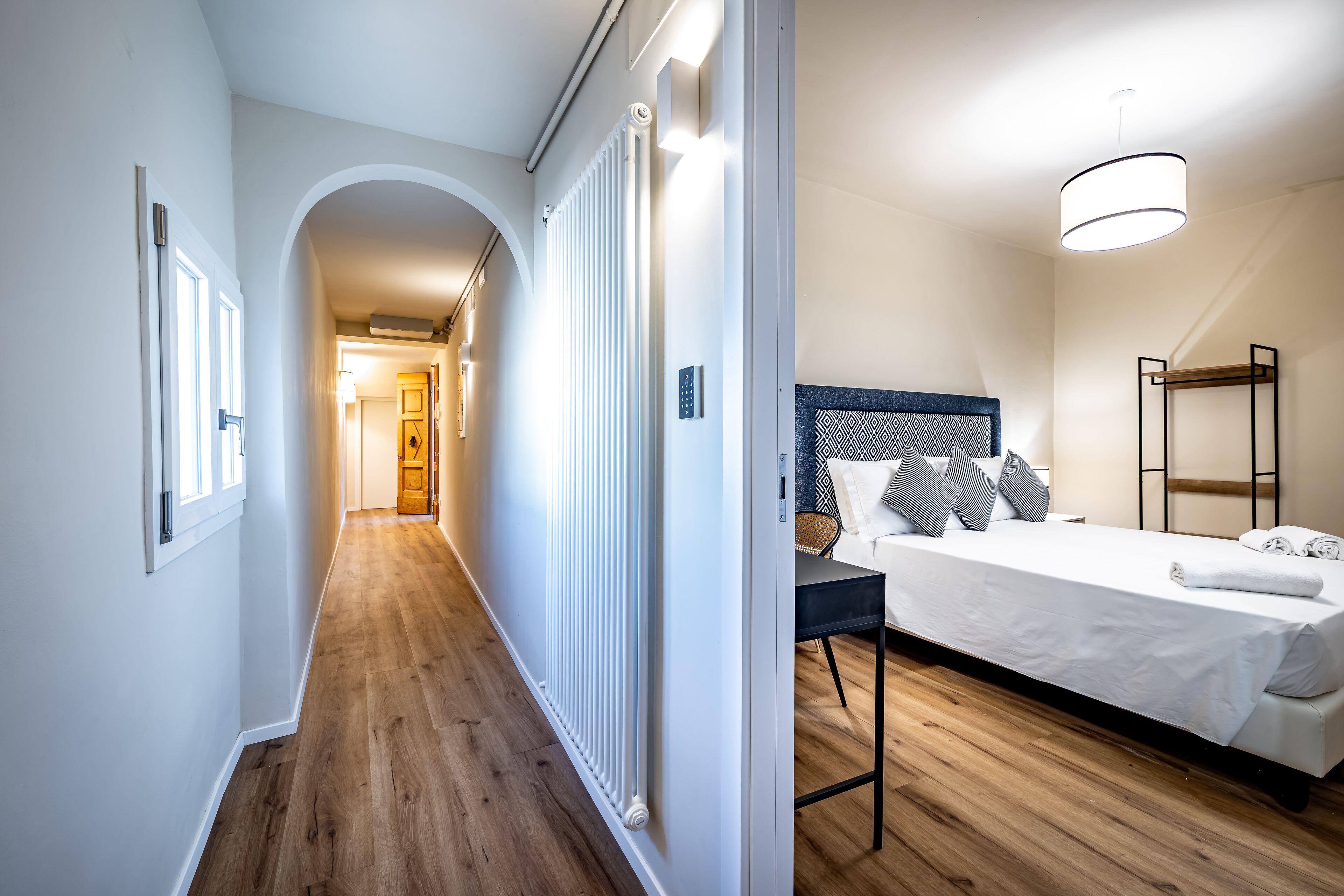 A hallway with a radiator, a bed with a headboard, and a bedside table.