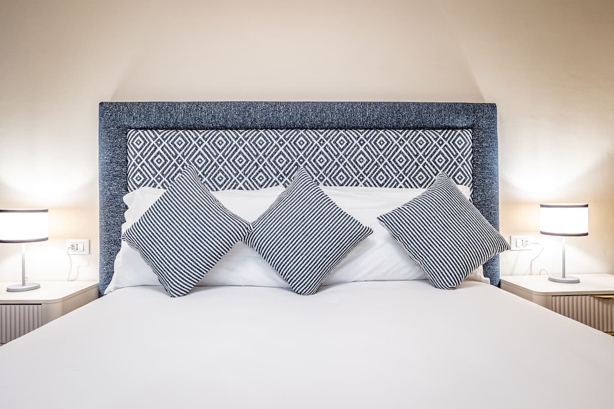 A neatly made bed with a patterned headboard and two bedside lamps.