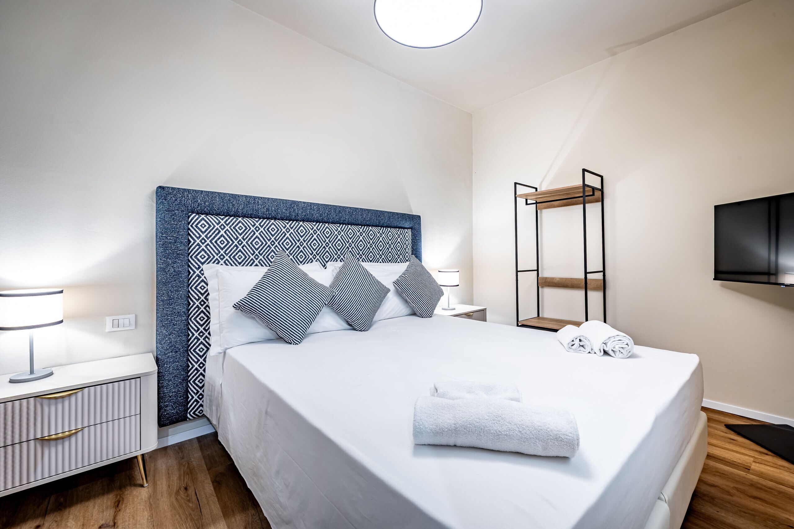 Une chambre d’hôtel moderne avec un grand lit, une table de chevet avec une lampe, un téléviseur fixé au mur et un plancher en bois.
