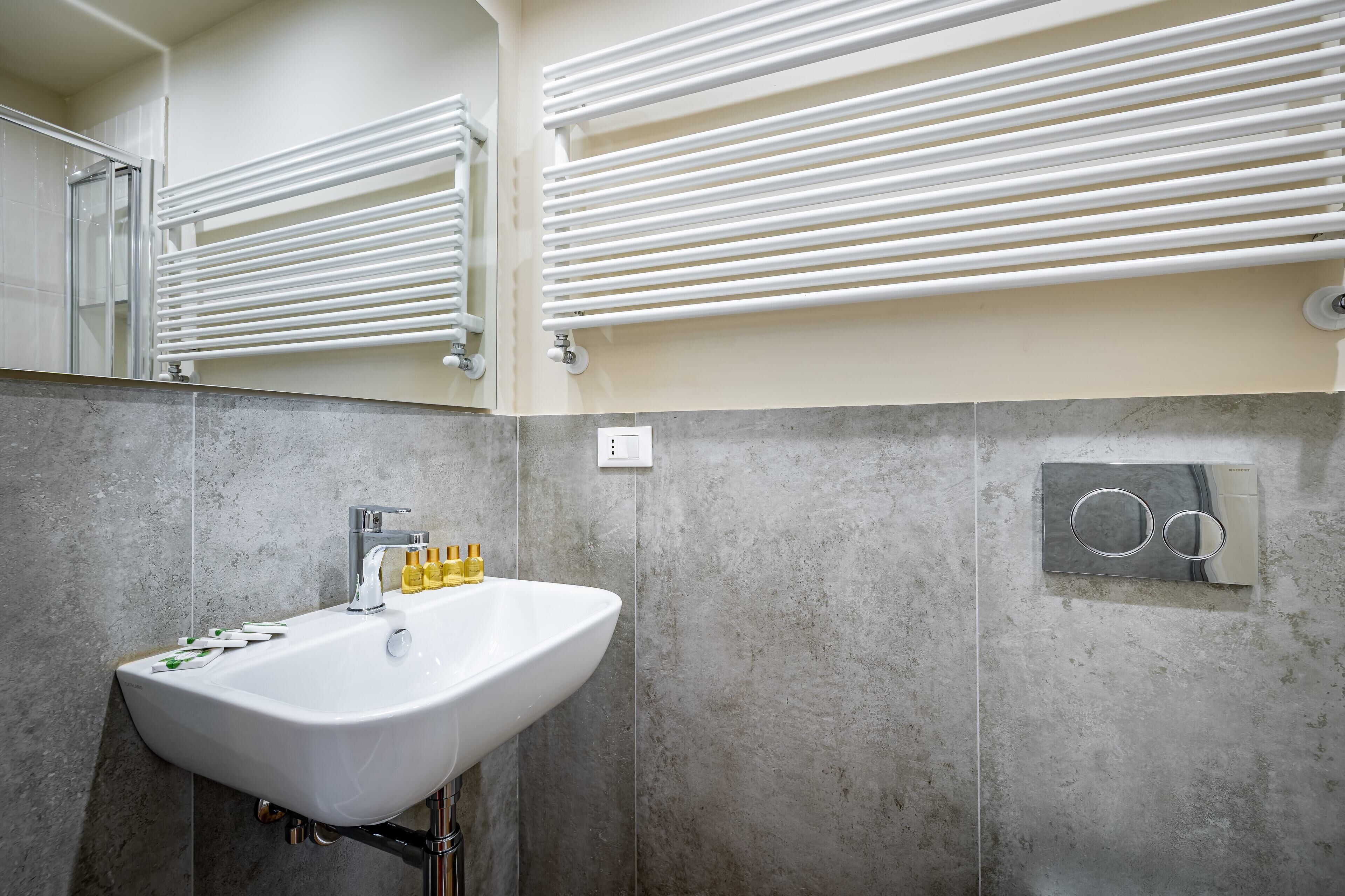 A bathroom with a white sink, mirror, towel racks, and a marble-tiled wall.