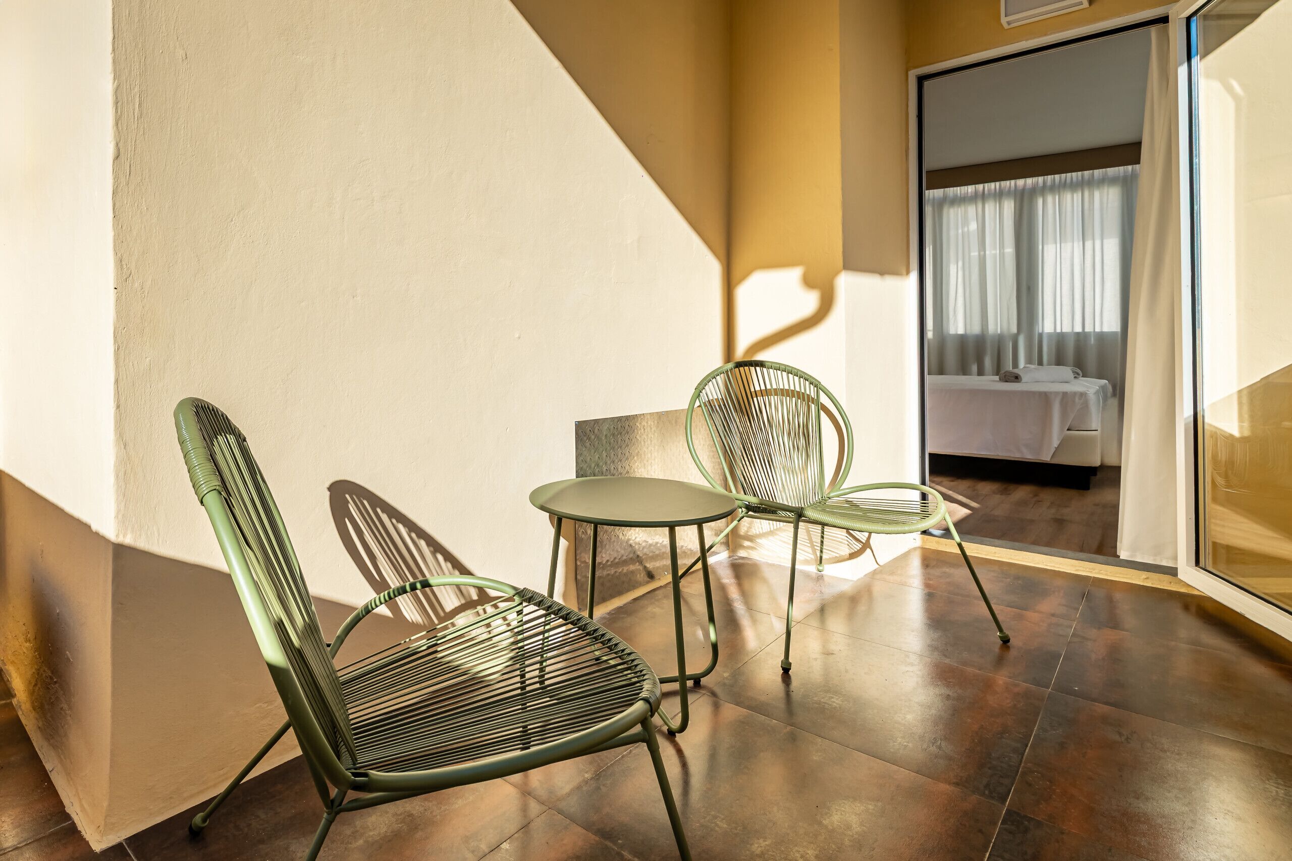 Une pièce comprenant un lit, deux chaises, une petite table et une porte vitrée donnant sur une autre pièce.