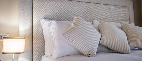 A neatly made bed with a patterned headboard, a bedside lamp, and a wall with a textured finish.