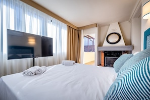 A hotel room with a bed, a flat-screen TV, a fireplace, and a balcony with a view.