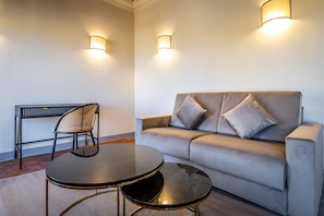 A modern room with a grey sofa, two black round tables, a wicker chair, and two wall-mounted lamps.