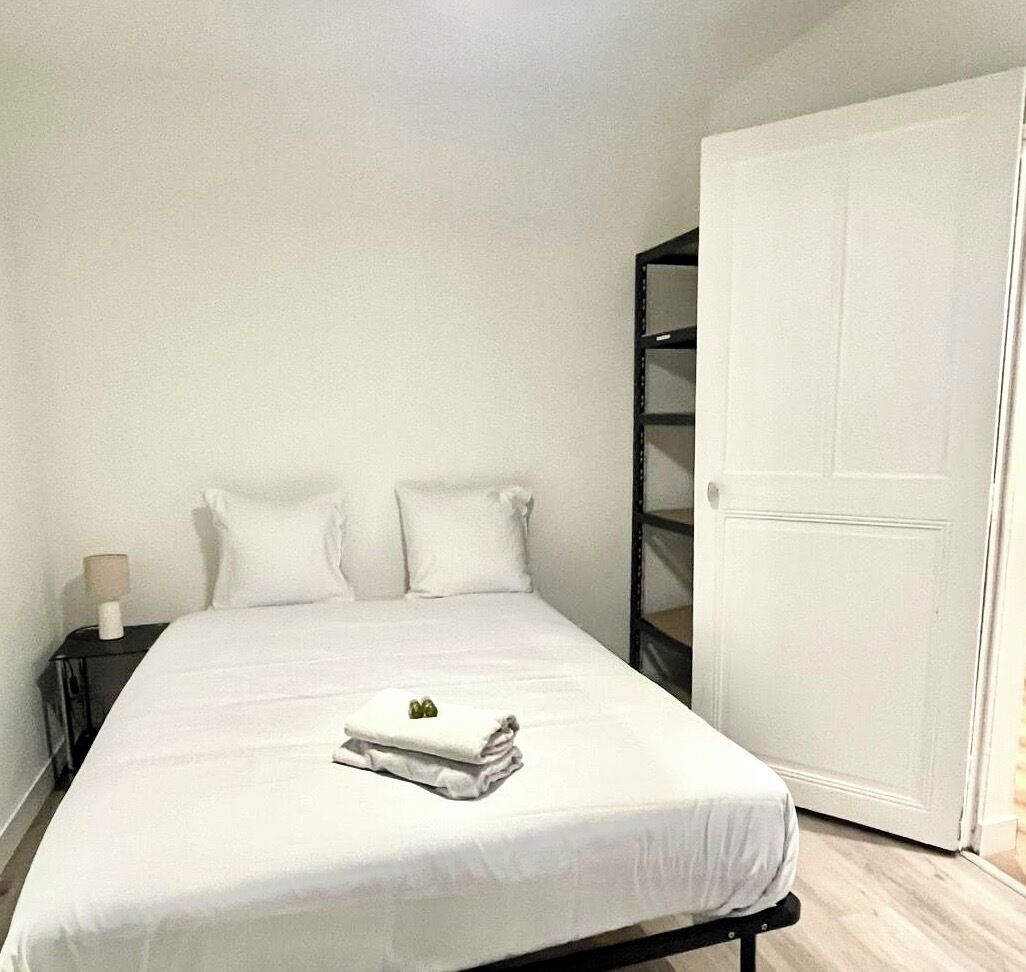 A neatly made bed with white bedding and pillows, a bedside lamp, and a closed door to the right.