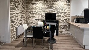 A compact kitchen with a stone wall, a dining table with chairs, a TV, and a microwave on a counter.