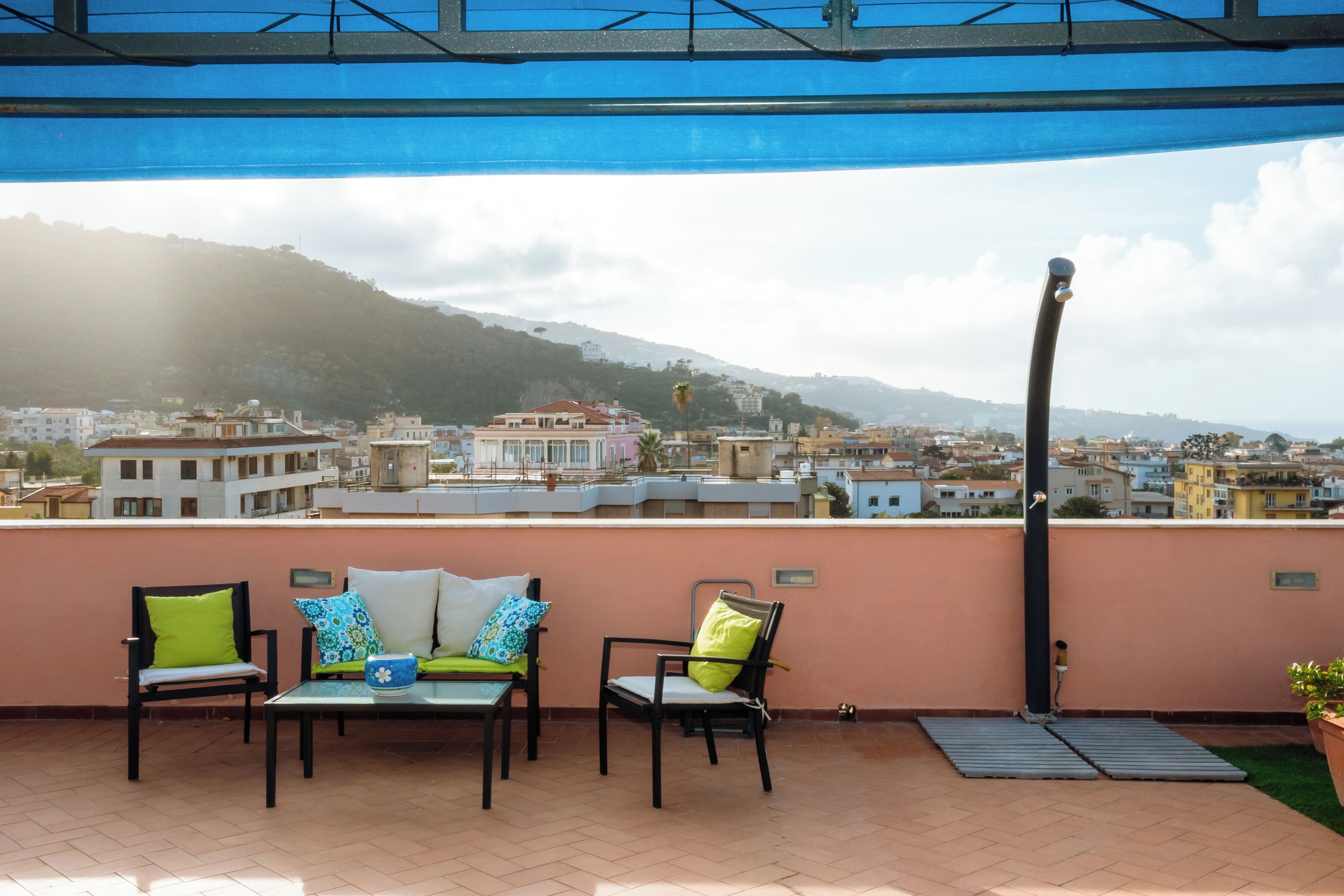 A rooftop terrace with two chairs and a table, overlooking a cityscape with buildings and hills.