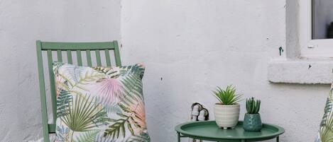 A green chair with a floral pillow, a small table with two potted plants, and a white wall.