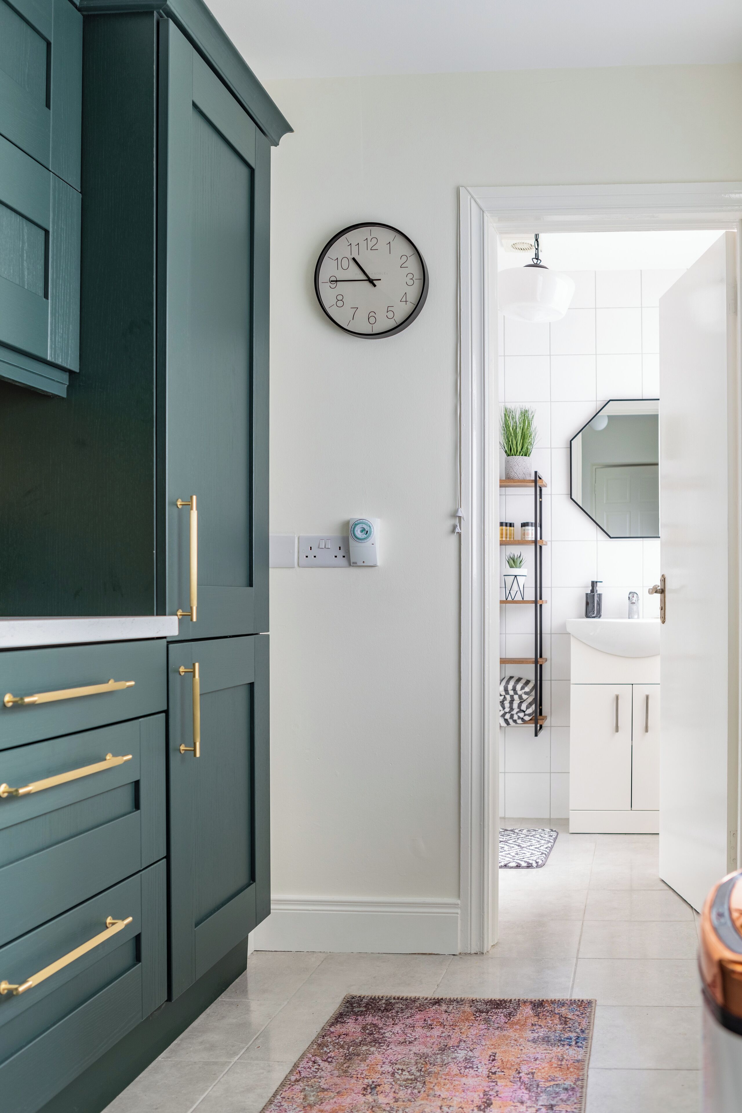 A modern kitchen with teal cabinets, a white countertop, and a clock on the wall.