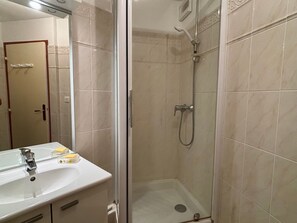 Ein Badezimmer mit einer Duschkabine, einem Waschbecken mit Spiegel und einer Tür zu einem anderen Raum.