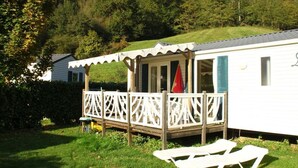 A mobile home with a porch, a small deck, and two lounge chairs.