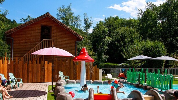 A wooden cabin with a pool area featuring slides and a water fountain.