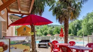 An outdoor seating area with red plastic chairs and tables, a red umbrella, and a pool in the background.