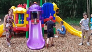 Um parquinho com um escorrega roxo, escorregas amarelos e azuis, e uma estrutura de escalada vermelha e verde.