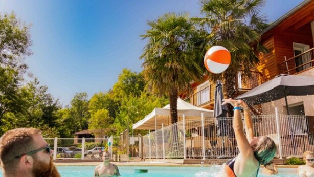 Área de piscina com palmeiras e um edifício de madeira ao fundo.