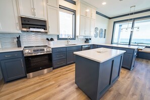 A modern kitchen with a central island, stainless steel appliances, and a view to the outside. - August 2026 Big Savings!!! RENOVATED & GORGEOUS BEACHFRONT (Eastpoint)