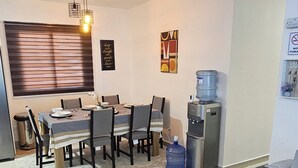 Una sala moderna con un sofá, una mesa de centro, una zona de comedor con una mesa y sillas, un dispensador de agua y un refrigerador.