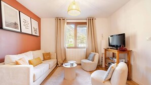 A cozy living room with a white sofa, a round coffee table, a white armchair, and a television on a wooden stand. - For large gatherings: 2 apartments under a welcoming roof (Taninges)