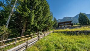 A wooden pathway leading to a mountain cabin with a view of a forest and mountains. - Charming Swiss chalet with stunning mountain views. (Grächen)