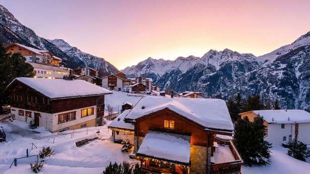 A snow-covered mountain village with wooden houses and a view of snow-capped peaks in the background. - Charming Swiss chalet with stunning mountain views. (Grächen)