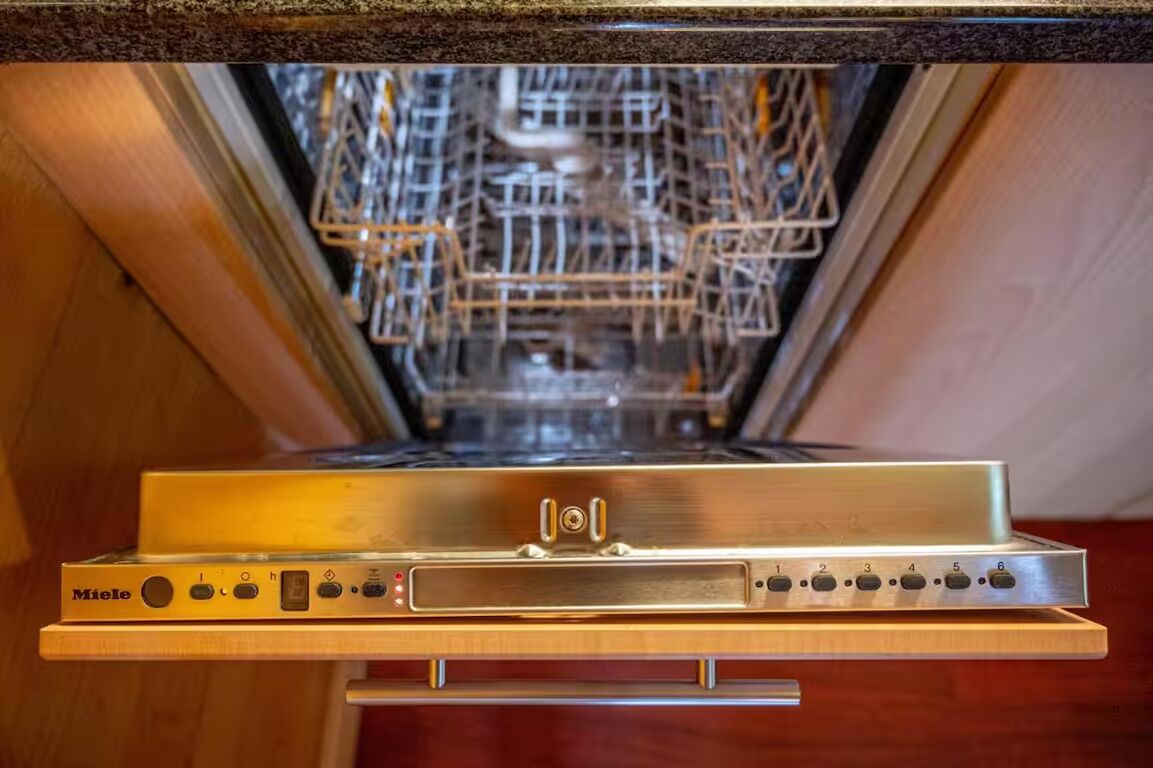 An open dishwasher with a control panel and a metal rack inside.