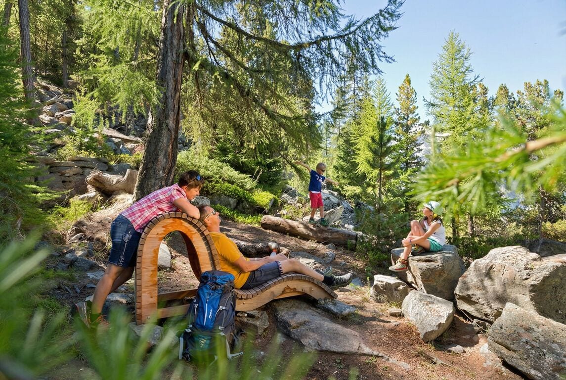Un banc en bois rustique, situé dans une zone boisée, avec des randonneurs à proximité.