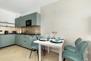 A dining table set with plates and green upholstered chairs. The kitchen is visible in the background, creating an open-plan feel. The setup looks ready for everyday use. - Elegant Apartment | Rooftop Pool | Close to the Beach (Mielno)