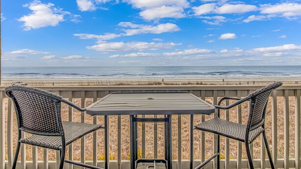 A deck with two chairs and a table overlooking a beach with waves and a clear sky. - I-2 2nd Floor Oceanfront with King Bed Suite (North Myrtle Beach)