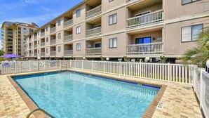A multi-story hotel with a swimming pool, balconies, and a fenced pool area. - I-2 2nd Floor Oceanfront with King Bed Suite (North Myrtle Beach)