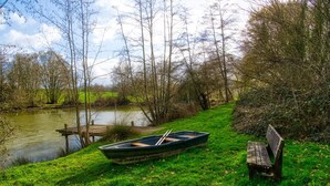 Uma área gramada com um píer, um barco e um banco à beira de um rio calmo.