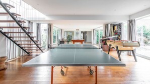 Um quarto amplo com mesa de pingue-pongue, mesa de futebol de botão e escada com cortinas listradas.