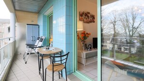 A balcony with a table and chairs, a refrigerator, a cabinet, and a window with a view of trees and a house. - Rated Apartment Au Clos Du Loc'h, Private Terrace with No Overlook (Pordic)