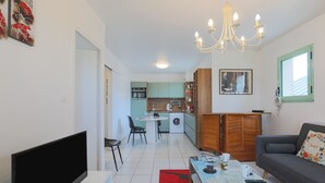 A compact living space with a flat-screen TV, a dining area, a kitchen with a washing machine, and a sofa with a floral pillow. - Rated Apartment Au Clos Du Loc'h, Private Terrace with No Overlook (Pordic)