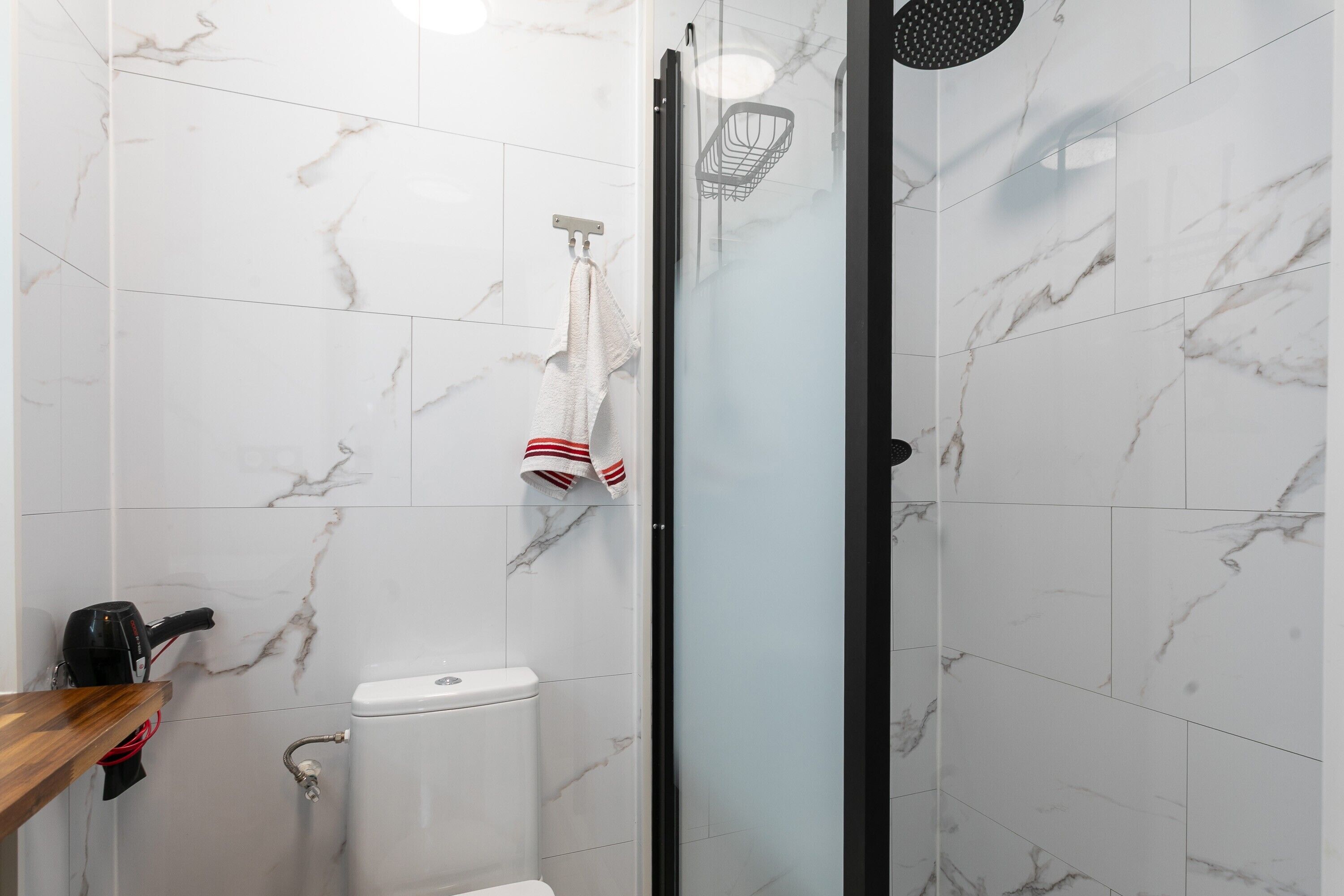 A bathroom with white marble tiles, a glass shower enclosure, a toilet, and a towel rack with a towel.