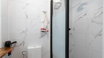 A bathroom with white marble tiles, a glass shower enclosure, a toilet, and a towel rack with a towel.