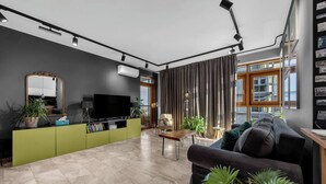 A modern living room with a large flat-screen TV, green entertainment unit, and a comfortable sofa. - Muranów 14th Floor Apt - 62m2, Parking, Balcony - by Rentujemy (Warszawa)