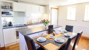 A modern kitchen with white cabinets, a dining area with a wooden table set for four, and a flower vase on the counter.