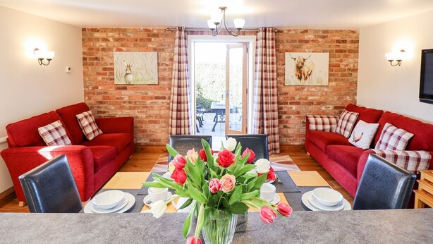 A cozy living room with two red sofas, a dining table with a vase of tulips, and brick walls with artwork.