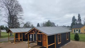 A small, single-story building with a metal roof, wooden exterior, and a porch area. - Relaxing fun bunk house 1 (Weyerhaeuser)
