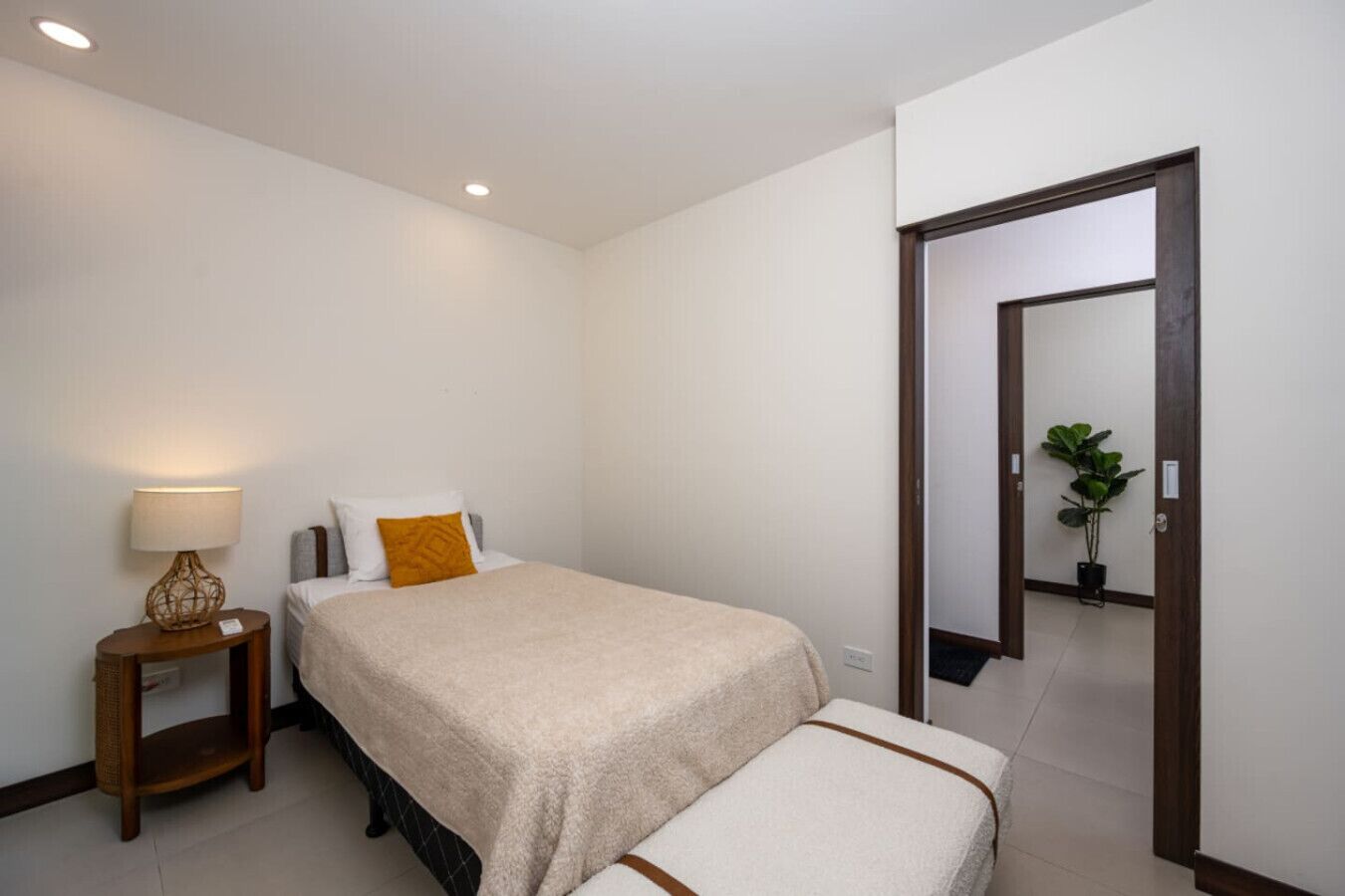 A bedroom with a bed, bedside table, lamp, and a mirror.